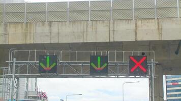 Signaling LED directional arrows and red X on Bangkok expressway ramp, set beneath a concrete overpass under a grey sky. photo