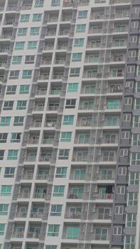 Tall residential building in Bangkok with rows of identical balconies and glass windows, showing typical urban living architecture under cloudy daylight. photo