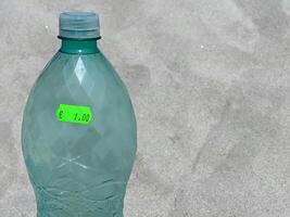 A plastic water bottle with 1 euro price sticker at the background of a beach sand on a hot summer day photo