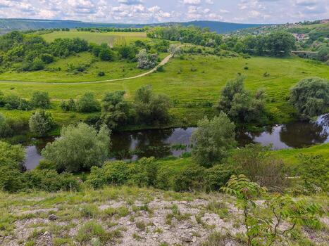 A lush green field with a river running through it. The river is calm and peaceful, and the surrounding trees add to the serene atmosphere. Concept of tranquility and natural beauty photo