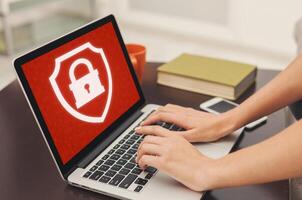 Blocked website or app and cyber security, ban or problems at work. Unrecognizable female hands typing on laptop enters login and password, at home or office with red screen and closed lock, close up photo