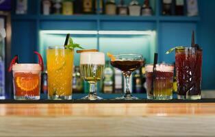 Closeup row of creative sweet exotic alcohol party cocktails in restaurant at bar background. Glasses with beverages on bar table, refreshing drinks with straws, night life concept photo