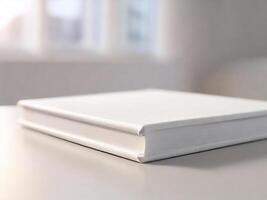 A white book sitting on a table in front of a window photo