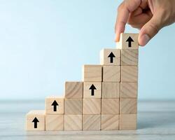 Hand stacking wooden blocks with upward arrows creating a growth staircase isolated on blue background photo