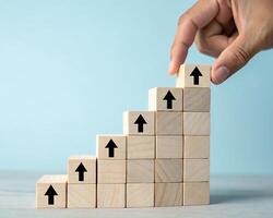 Hand placing a wooden block with an upward arrow on a staircase of blocks isolated on white background photo