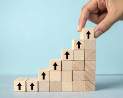 Hand placing a wooden block with an upward arrow on a stair like structure isolated on white background photo