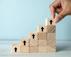 Hand placing wooden block with upward arrow on stair step isolated on white background photo