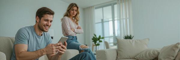 a cheerful man is texting someone on his smartphone, his sad wife is next to him in the apartment photo
