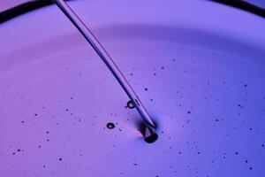 A jet of facial oil flowing into a petri dish on a purple background. photo