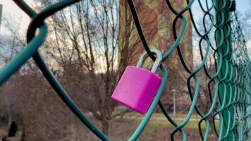 A pink padlock is attached to a chain link fence video