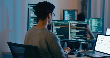 Ásia macho, fêmea freelance digitando escrever pronto ai robô isto aplicativo inteligente programa nômade, jogo, terminal com codificação linguagem, desenhista, grande dados Centro em Área de Trabalho computador dentro noite escritório. video