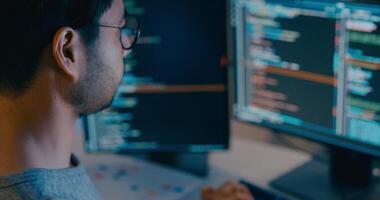 Ásia masculino freelance digitando escrever pronto ai robô isto aplicativo inteligente programa nômade, jogo, terminal com codificação linguagem, desenhista, grande dados Centro em Área de Trabalho computador dentro noite escritório. video