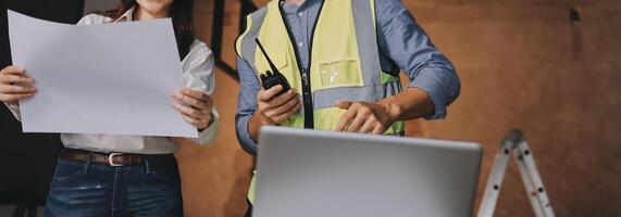 Two people in safety vests holding papers and looking at a laptop photo
