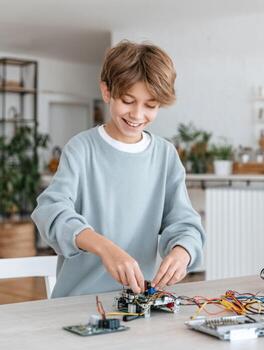 chico montaje electrónico circuito con alambres y componentes, sonriente y enfocado en proyecto en brillante habitación foto