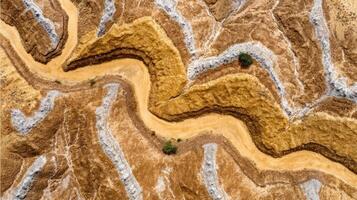 Winding dirt road through dry rugged terrain with sparse vegetation and contrasting earth tones creating abstract natural pattern photo