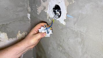 A hand connects colorful wires amid rustic concrete, sparking DIY renovation magic for International Craft Month celebrations photo