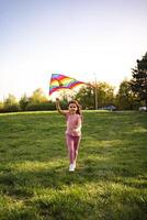 Joyful girl runs with colorful kite in sunny park photo