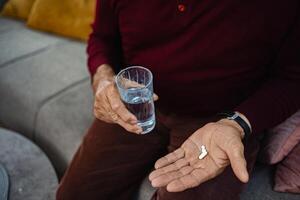 Older man taking medication with glass of water at home photo