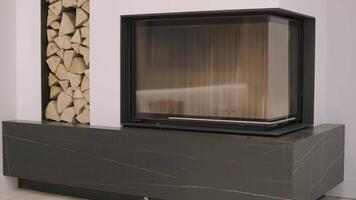 Sleek modern fireplace with a glass door and adjacent stacked firewood, combining functionality and design in a contemporary living space video