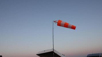 windsock blowing in evening breeze showing wind direction on airfield with clear gradient sky and vehicle roof below, concept of aviation, weather forecasting, flight school video
