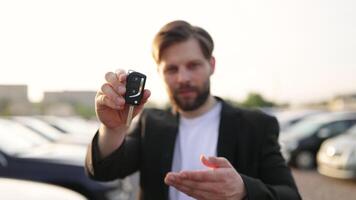 A businessman holds up a car key, smiling at the camera. He appears to be at a car dealership, with cars in the background. video