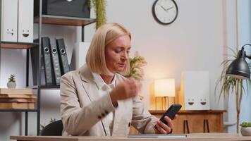 decepcionado maduro mujer de negocios leer malo Noticias en teléfono inteligente a hogar oficina mesa. triste hembra en formal traje trastornado por desagradable notificación, conmocionado por información en Internet, Deprimido por mensaje video