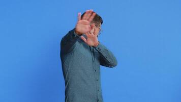 Don't want to look at this, awful. Afraid shocked Caucasian middle-aged man in glasses closing eyes with hand showing stop gesture, confused shy scared reject to watch. Guy isolated on blue background video