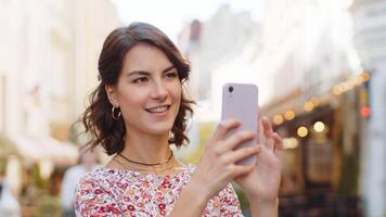 caucásico bonito mujer tomando fotografía imágenes de antiguo ciudad edificios al aire libre. adulto niña blogger utilizando teléfono inteligente fotografía aplicación haciendo fotos para social medios de comunicación en pie en calle. pueblo estilo de vida video
