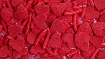 närbild av röd hjärtformade godis och strössel roterande, skapande en vibrerande, texturerad mönster i ljus belysning video