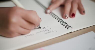 portátil fechar acima tomada, uma mulher é levando notas dentro uma caderno enquanto sentado às uma escrivaninha preenchidas com o negócio gráficos e pegajoso notas. video