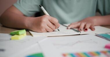 handhållen selektiv fokus skott, en kvinna är tar anteckningar i en anteckningsbok medan Sammanträde på en skrivbord fylld med företag diagram och klibbig anteckningar. video