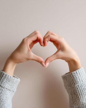 Hands Forming Heart Shape in Cozy Sweater Against Neutral Wall photo
