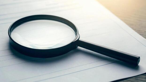 Magnifying glass document paper black handle closeup investigation search analysis sunlight focus study office desk reading photo