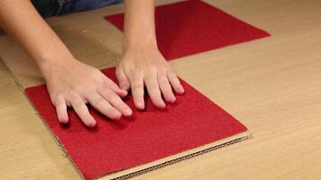 mani accuratamente posto rosso carta vetrata lenzuola su un' cartone superficie, dimostrando un' preciso e metodico preparativi tecnica video