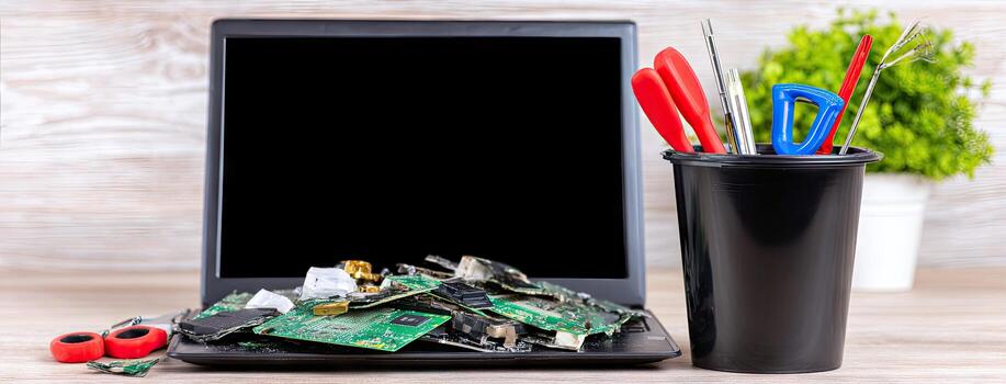 Laptop with broken screen and electronic components on wooden table photo