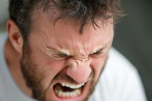 A man with a beard and a white shirt is making an angry face photo