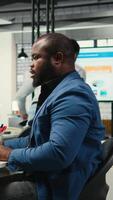 vertical negro empresario de corrección su malo postura a el puesto de trabajo, relación comercial con espalda y cuello músculo dolor debido a intenso trabajar. administrador resolviendo Tareas para productividad y eficiencia. cámara una. video