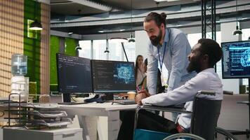 Manager supervising developer with paraplegia writing code, developing deep learning APIs. Supervisor overseeing work done by IT expert in wheelchair troubleshooting software errors using AI, camera A video