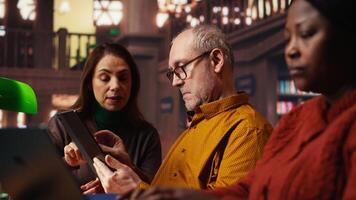 adulto personas estudiando juntos en un instalaciones biblioteca y transcribiendo lecciones, concentrando en papeleo y demostración su compromiso a investigando preparando para Universidad tesis. cámara b. video