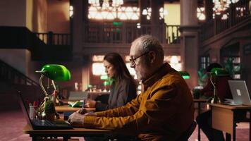 focalizzata anziano persona lettura ragnatela educativo documenti nel un' Università biblioteca, commesso per completando il suo studi e raggiungimento un' significativo grado nel il suo dopo anni. vecchio uomo. telecamera un. video