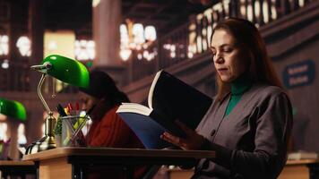Mature woman reading and writing at a university campus library, working on thesis with intellectual ambition and dedication for life long learning and personal achievement. Camera B. video