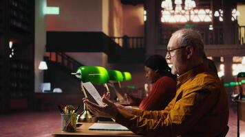 experimentado hombre ensayando un teatro guión en un tranquilo biblioteca, estudiando líneas con compromiso y emoción y practicando personaje desarrollo para papel preparación. interino habilidades. cámara una. video