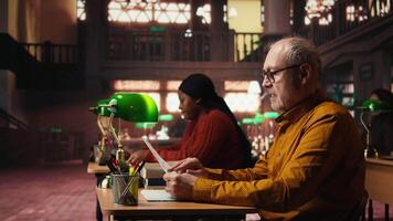 åldrig man i en studie område omgiven förbi bibliotek böcker och pappersarbete, framställning för universitet kurser och avhandling skrivning med akademisk databas material på de campus. kamera a. video