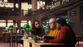 Mature team of people reviewing materials and class work for university degree, surrounded by academic archived documents and books. Quiet atmosphere of learning in study area. Camera A. video