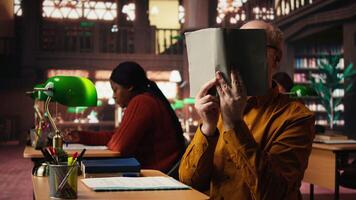 sabio Envejecido persona leyendo un libro a el público biblioteca y disfrutando gratis tiempo, teniendo un clásico pasatiempo de ganando conocimiento durante Jubilación. contento relajado pensionista con gafas. cámara una. video