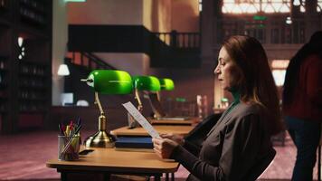 maduro estudiante en un estudiar habitación rodeado por libros y papeleo, preparando para Universidad trabajo de curso y tesis escribiendo, demostrando intelectual compromiso a educación. cámara una. video