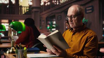 gammal person med glasögon åtnjuter läsning en bok på de bibliotek, varelse Lycklig och njuter rekreation. åldrig man med bok läsning hobby, pensionering fritid aktivitet i tyst Plats. kamera a. video