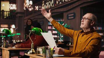 ouderen acteur in een bibliotheek scherpstellen Aan script lezing en memoriseren, voorbereidingen treffen voor een klassiek drama Speel met toewijding en passie voor theater prestatie. dramatisch kunsten. camera a. video