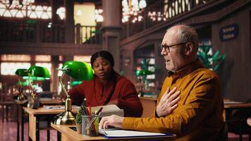 äldre högskola studerande gör andas in andas ut övning på grund av till fysisk obehag, har en respiratorisk problem i ångest på de bibliotek skrivbord. åldrig man sjuk i ångest. kamera a. video