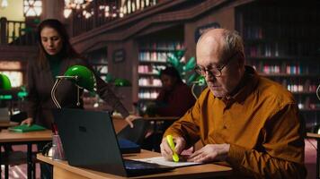 anziano alunno utilizzando evidenziatore penna per memorizzare lezione documenti, l'applicazione un' studia strategia con essenziale informazione a partire dal corsi. vecchio uomo lavori su memorizzazione per esami. telecamera un. video